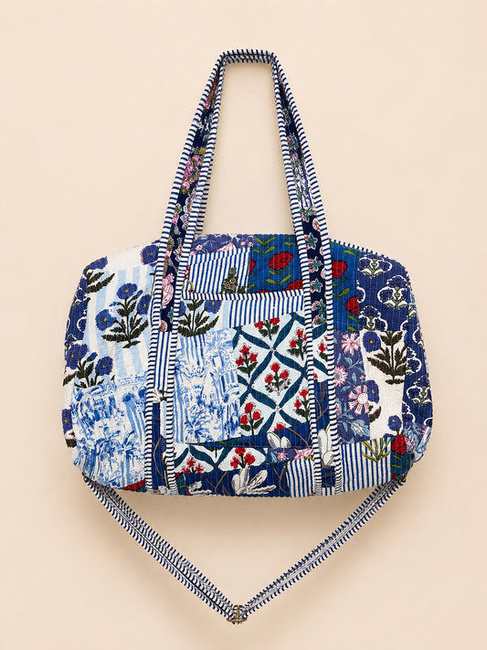 Model carrying a handmade patchwork duffle bag in a colorful flower field under a bright blue sky.