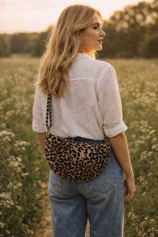 Handmade cross body bag Elara Wildflower Path in LEOPARD PRINT worn by woman in a field.