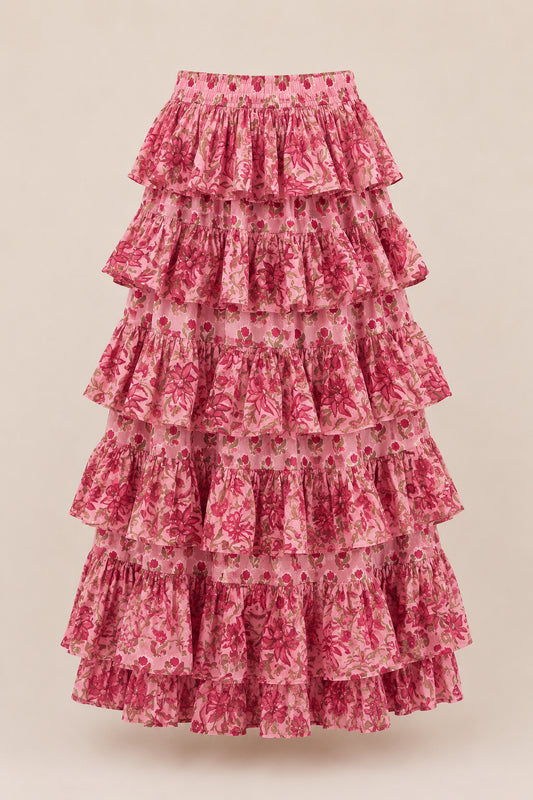Model in handcrafted tiered maxi skirt standing among pink flowers under a blue sky.