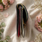 Handmade Leather Crossbody bag - Mira in black, pink, and red, surrounded by flowers on a linen background.