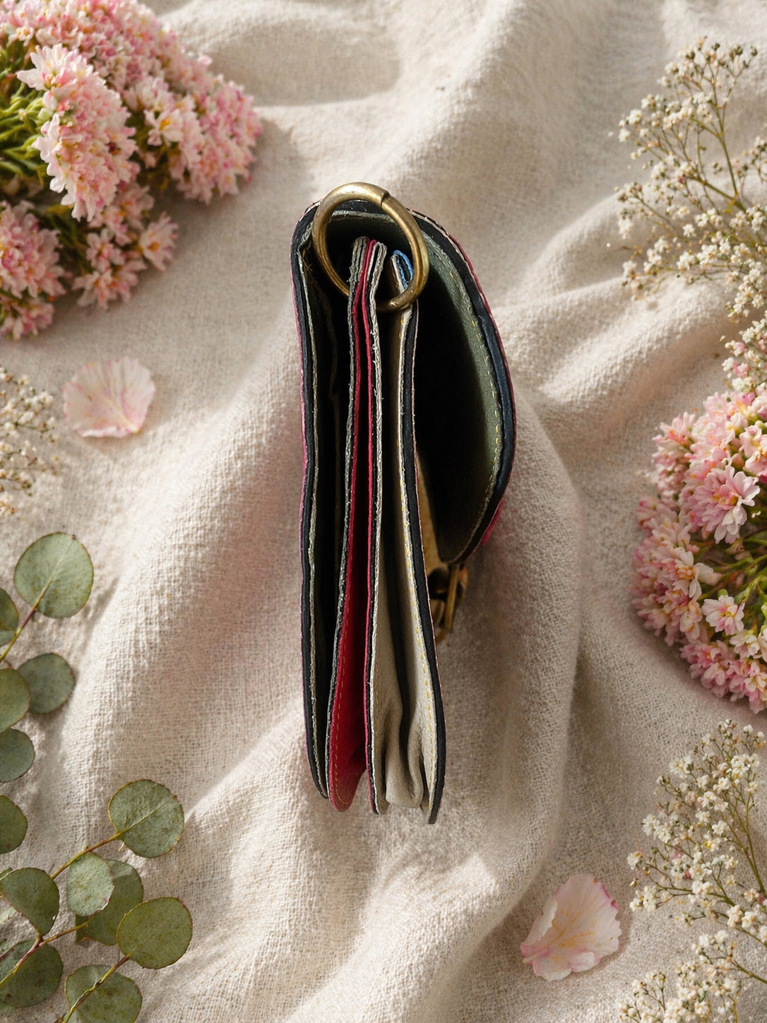 Handmade Leather Crossbody bag - Mira in black, pink, and red, surrounded by flowers on a linen background.