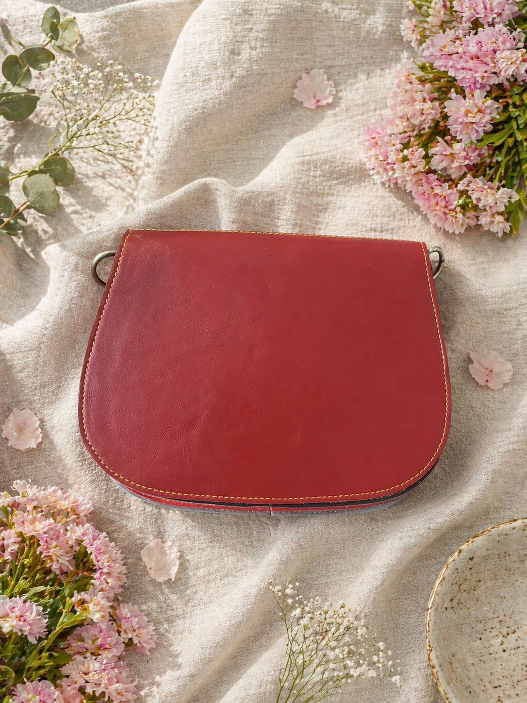 Handmade Leather Crossbody bag - Mira in black, pink, and red, surrounded by flowers on a linen background.