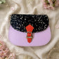 Handmade Leather Crossbody bag - Mira in black, pink, and red, surrounded by flowers on a linen background.