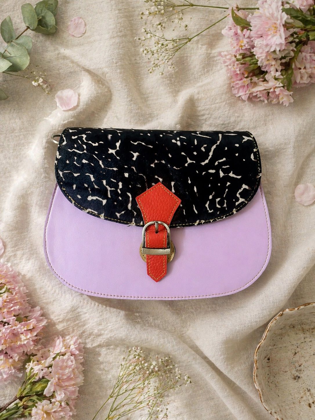 Handmade Leather Crossbody bag - Mira in black, pink, and red, surrounded by flowers on a linen background.