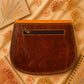 A Handmade Leather Crossbody Bag with vibrant colors, featuring an orange, green, and purple design, surrounded by floral accents.