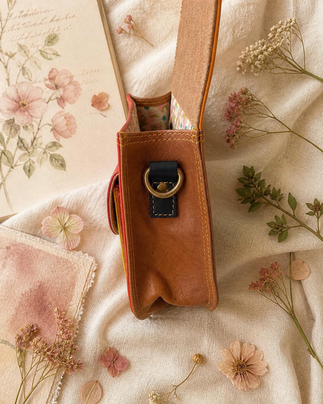 A Handmade Leather Crossbody Bag with vibrant colors, featuring an orange, green, and purple design, surrounded by floral accents.