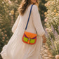 A Handmade Leather Crossbody Bag with vibrant colors, featuring an orange, green, and purple design, surrounded by floral accents.