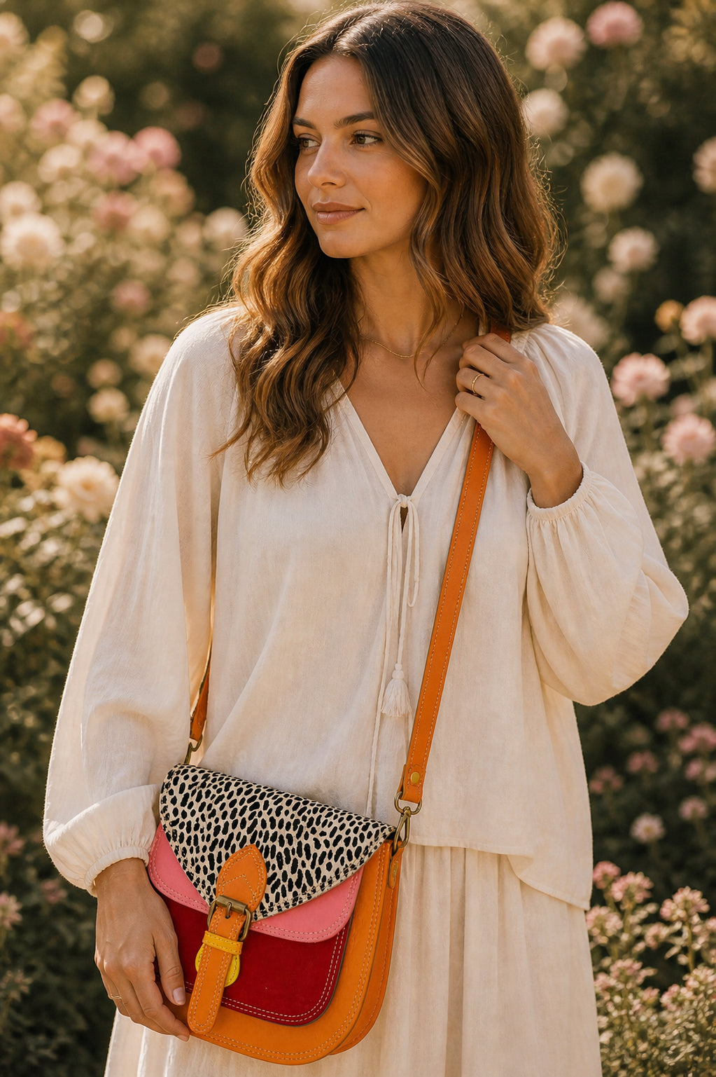 Handmade Leather Crossbody Bag - Romy in a model's hands, showcasing its unique design and vibrant colors against a floral backdrop.