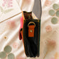 Handmade Leather Crossbody Bag - Romy in a model's hands, showcasing its unique design and vibrant colors against a floral backdrop.