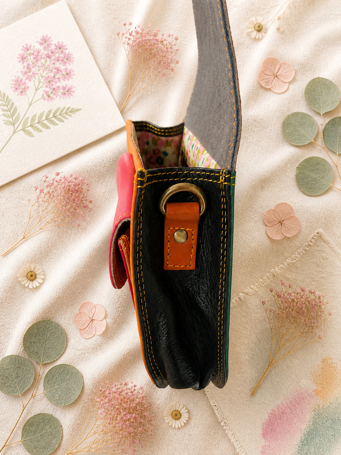 Handmade Leather Crossbody Bag - Romy in a model's hands, showcasing its unique design and vibrant colors against a floral backdrop.