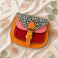 Handmade Leather Crossbody Bag - Romy in a model's hands, showcasing its unique design and vibrant colors against a floral backdrop.