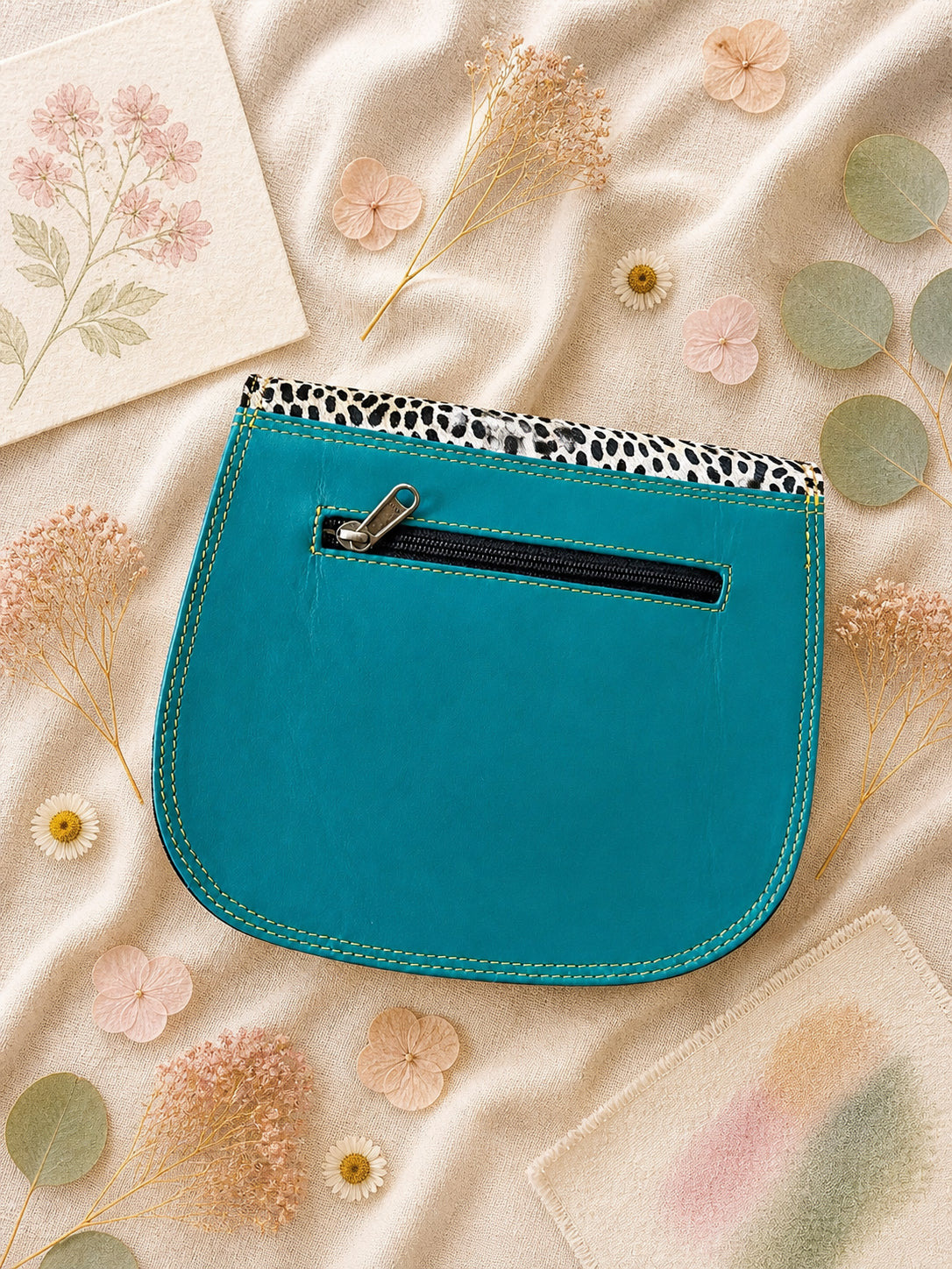 Handmade Leather Crossbody Bag - Romy in a model's hands, showcasing its unique design and vibrant colors against a floral backdrop.