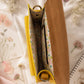 Handmade Leather Crossbody Bag - Romy in yellow and blue, surrounded by flowers and sketchbook.