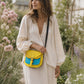 Handmade Leather Crossbody Bag - Romy in yellow and blue, surrounded by flowers and sketchbook.