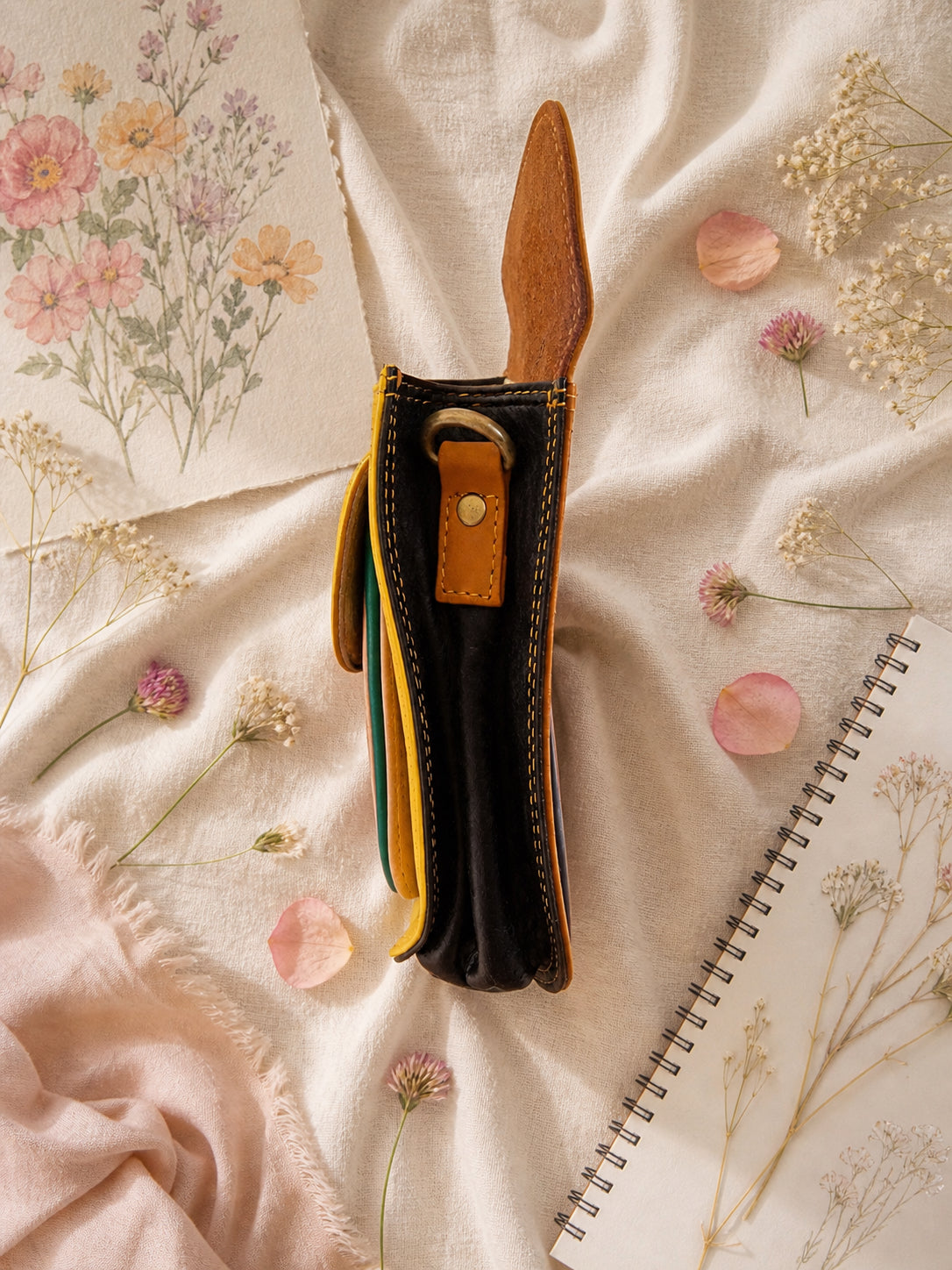 Handmade Leather Crossbody Bag - Romy in yellow and blue, surrounded by flowers and sketchbook.