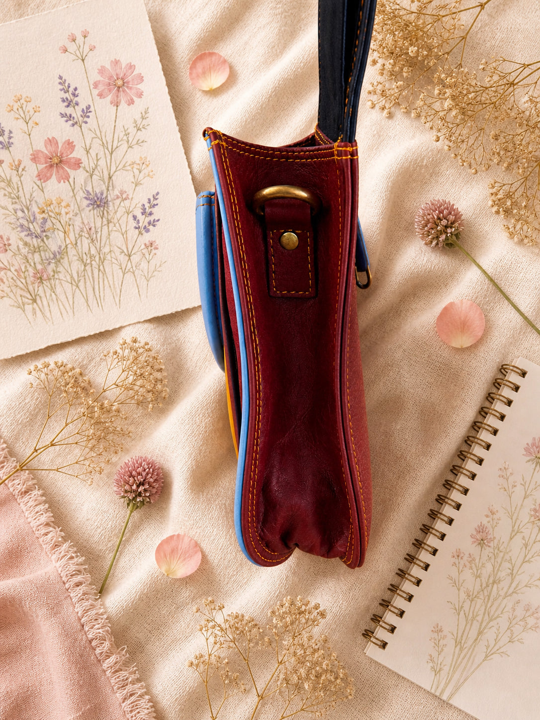 Handmade Leather Crossbody Bag in vibrant colors with pink, blue, and yellow hues, resting on a soft fabric backdrop.
