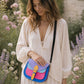Handmade Leather Crossbody Bag in vibrant colors with pink, blue, and yellow hues, resting on a soft fabric backdrop.
