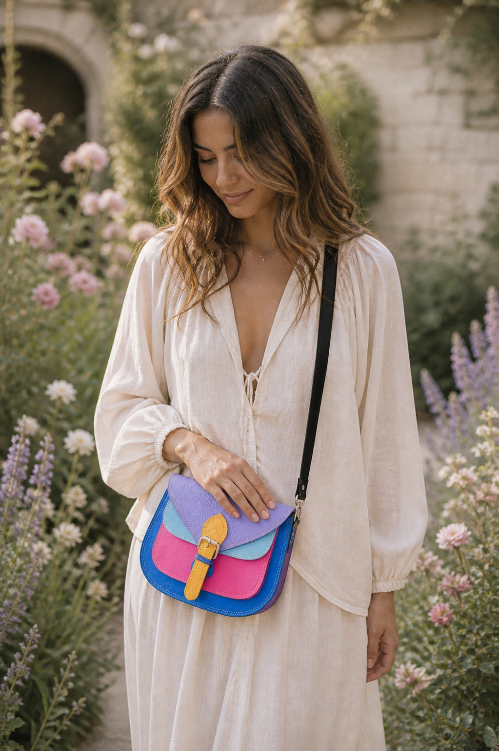 Handmade Leather Crossbody Bag in vibrant colors with pink, blue, and yellow hues, resting on a soft fabric backdrop.