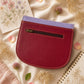 Handmade Leather Crossbody Bag in vibrant colors with pink, blue, and yellow hues, resting on a soft fabric backdrop.