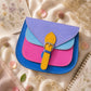 Handmade Leather Crossbody Bag in vibrant colors with pink, blue, and yellow hues, resting on a soft fabric backdrop.