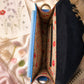 Handmade Leather Crossbody Bag in vibrant colors with pink, blue, and yellow hues, resting on a soft fabric backdrop.