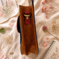 Handmade Leather Crossbody Bag - Romy - Painted Garden - Stardust displayed on a soft fabric with flowers and sketches.