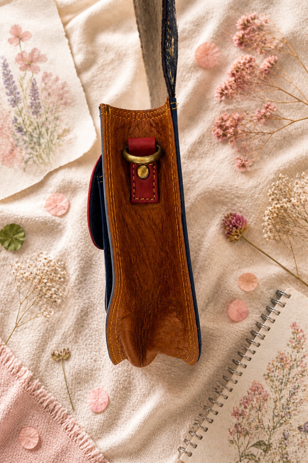 Handmade Leather Crossbody Bag - Romy - Painted Garden - Stardust displayed on a soft fabric with flowers and sketches.