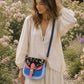 Handmade Leather Crossbody Bag - Romy - Painted Garden - Stardust displayed on a soft fabric with flowers and sketches.