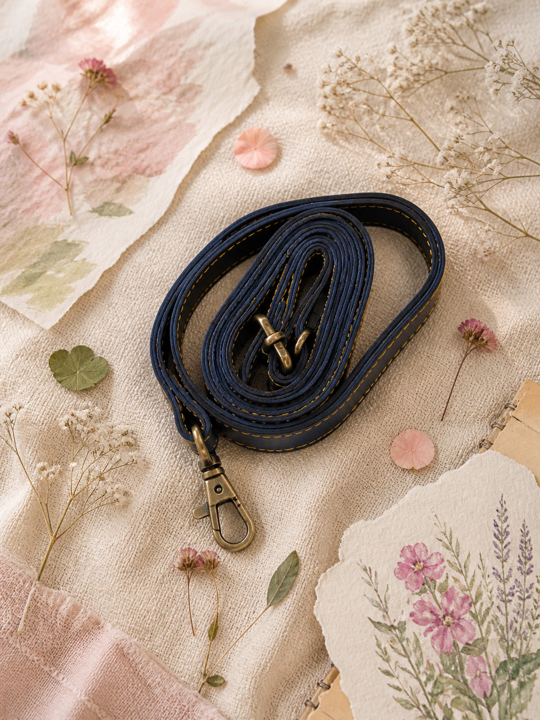 Handmade Leather Crossbody Bag - Romy - Painted Garden - Stardust displayed on a soft fabric with flowers and sketches.
