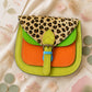 Handmade Leather Crossbody Bag in vibrant colors with leopard print flap on a textured background.