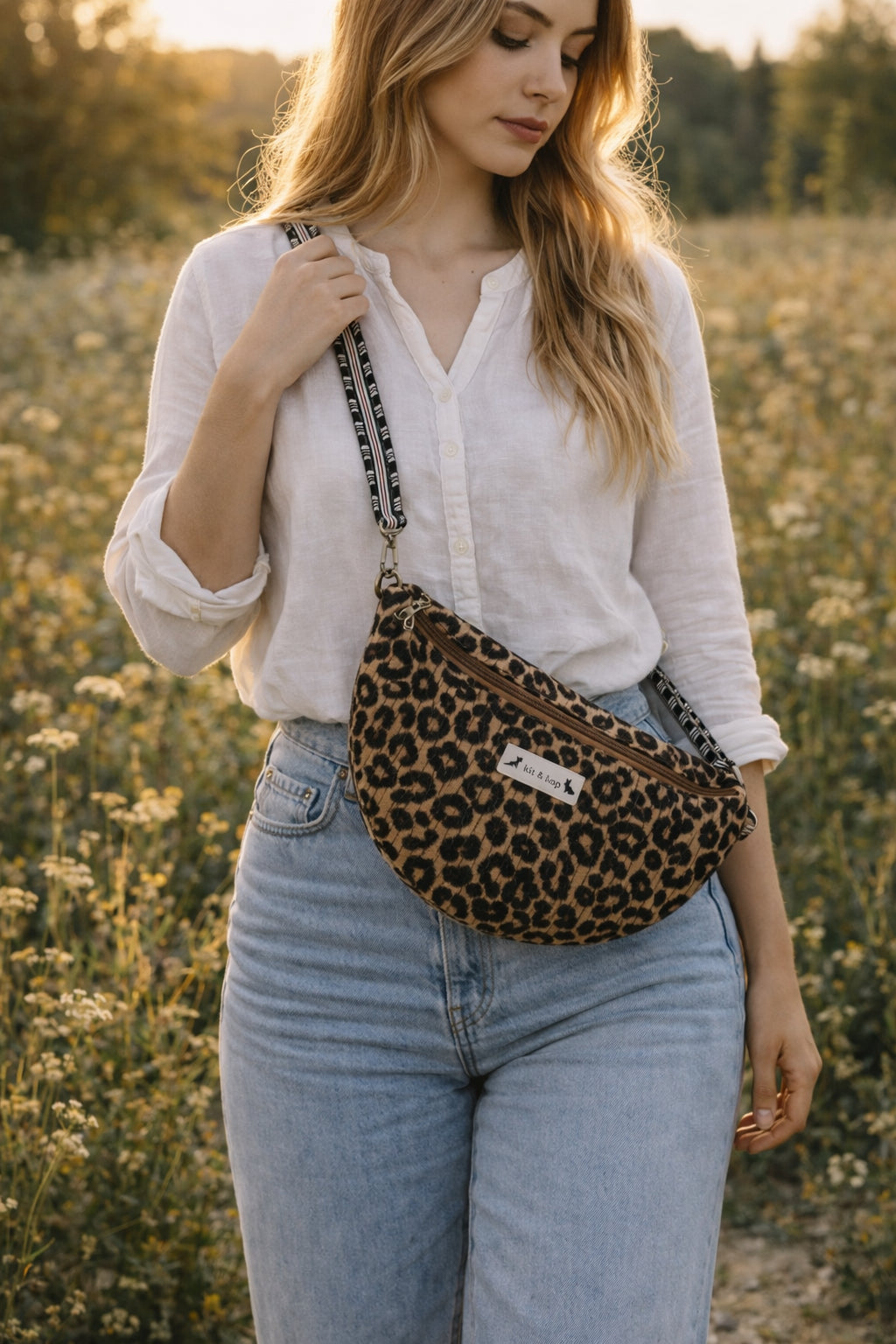 Handmade cross body bag Elara Wildflower Path in LEOPARD PRINT worn by woman in a field.