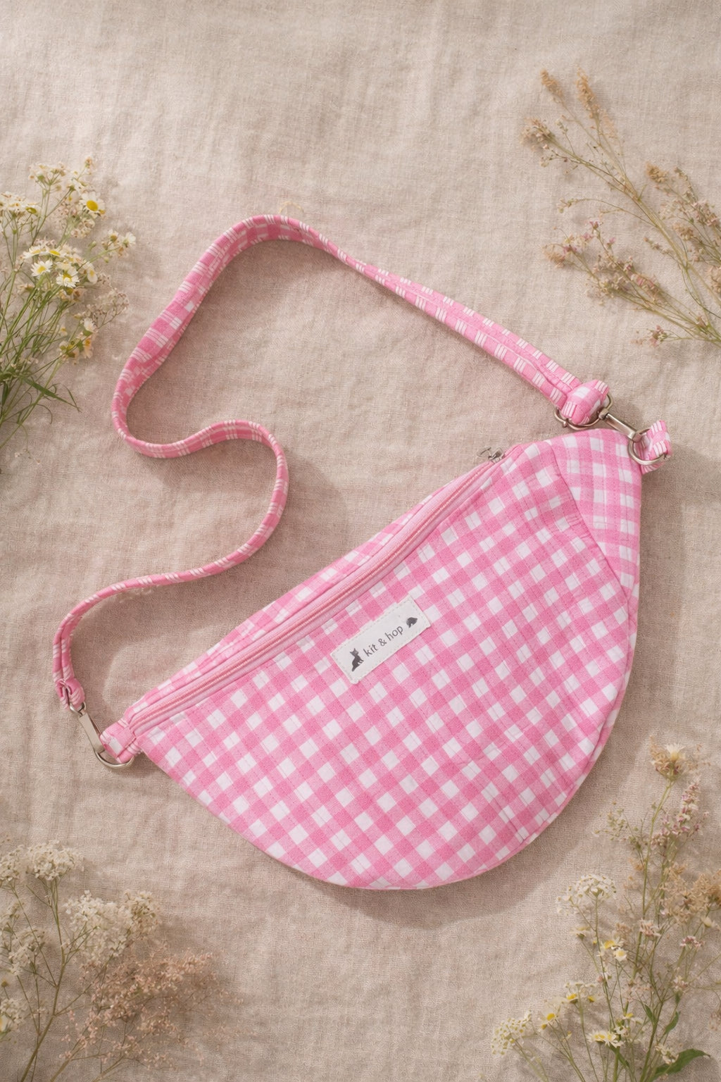 Handmade cross body bag Elara in pink gingham worn by a woman outdoors in a sunny field.