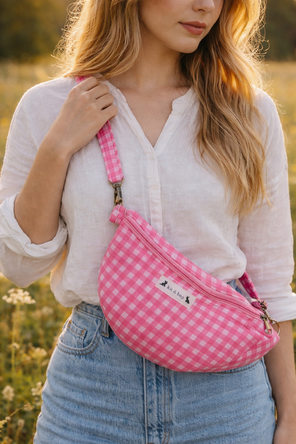 Handmade cross body bag Elara in pink gingham worn by a woman outdoors in a sunny field.