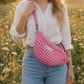 Handmade cross body bag Elara in pink gingham worn by a woman outdoors in a sunny field.