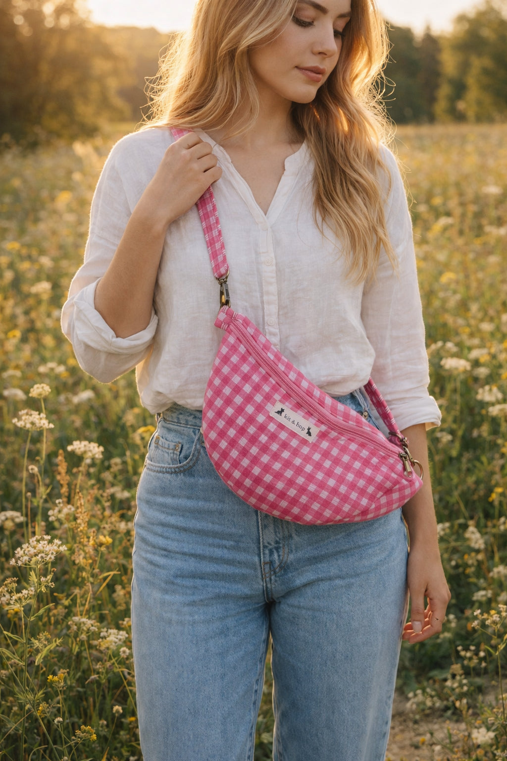 Handmade cross body bag Elara in pink gingham worn by a woman outdoors in a sunny field.