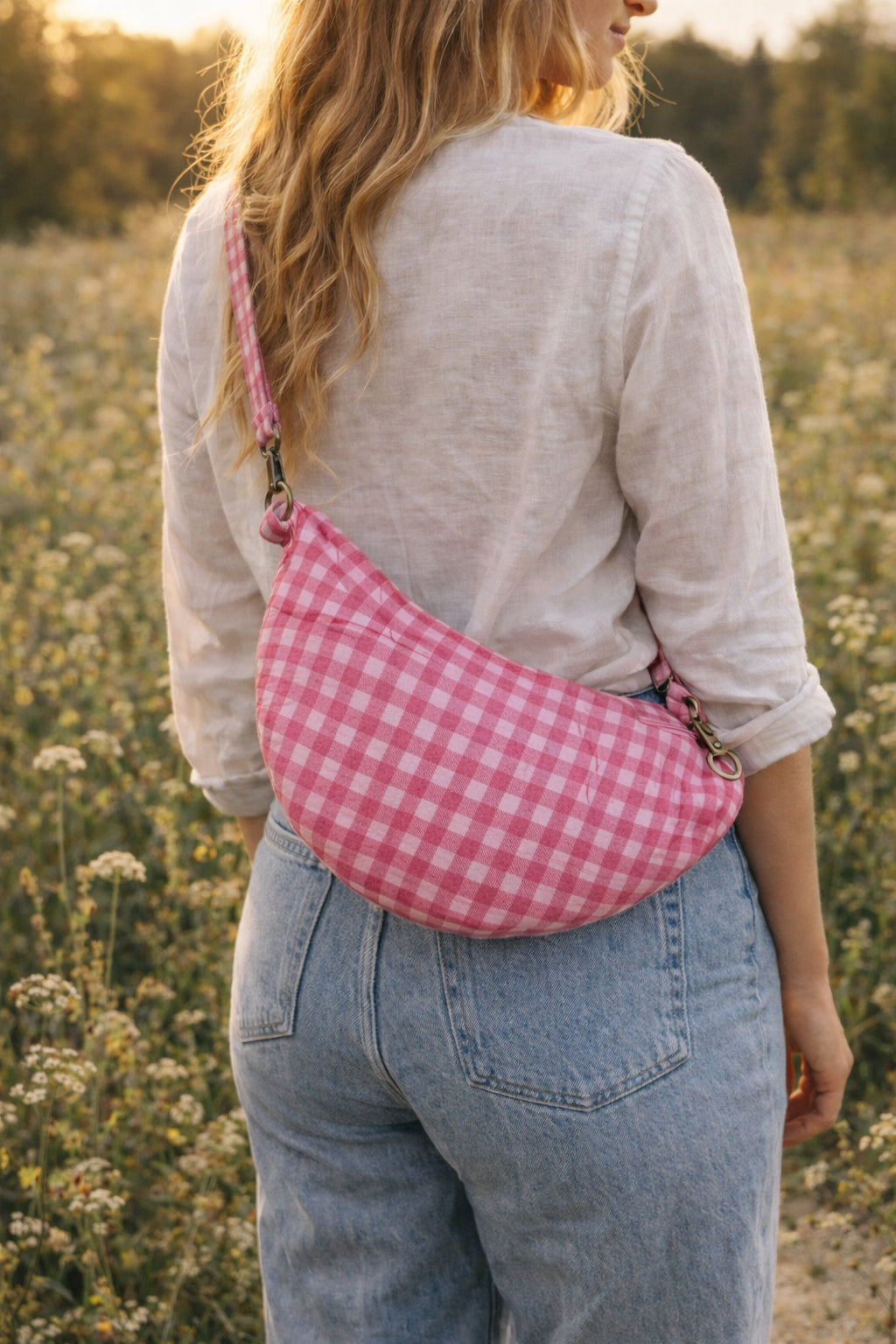 Handmade cross body bag Elara in pink gingham worn by a woman outdoors in a sunny field.
