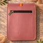 Handmade Leather Crossbody Bag in vibrant pink and orange tones, set against a textured background with greenery.