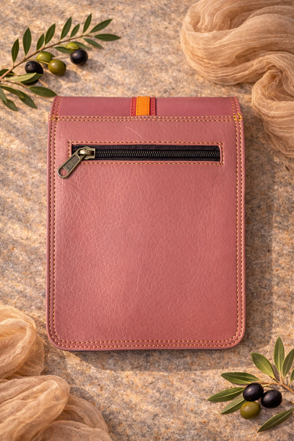 Handmade Leather Crossbody Bag in vibrant pink and orange tones, set against a textured background with greenery.