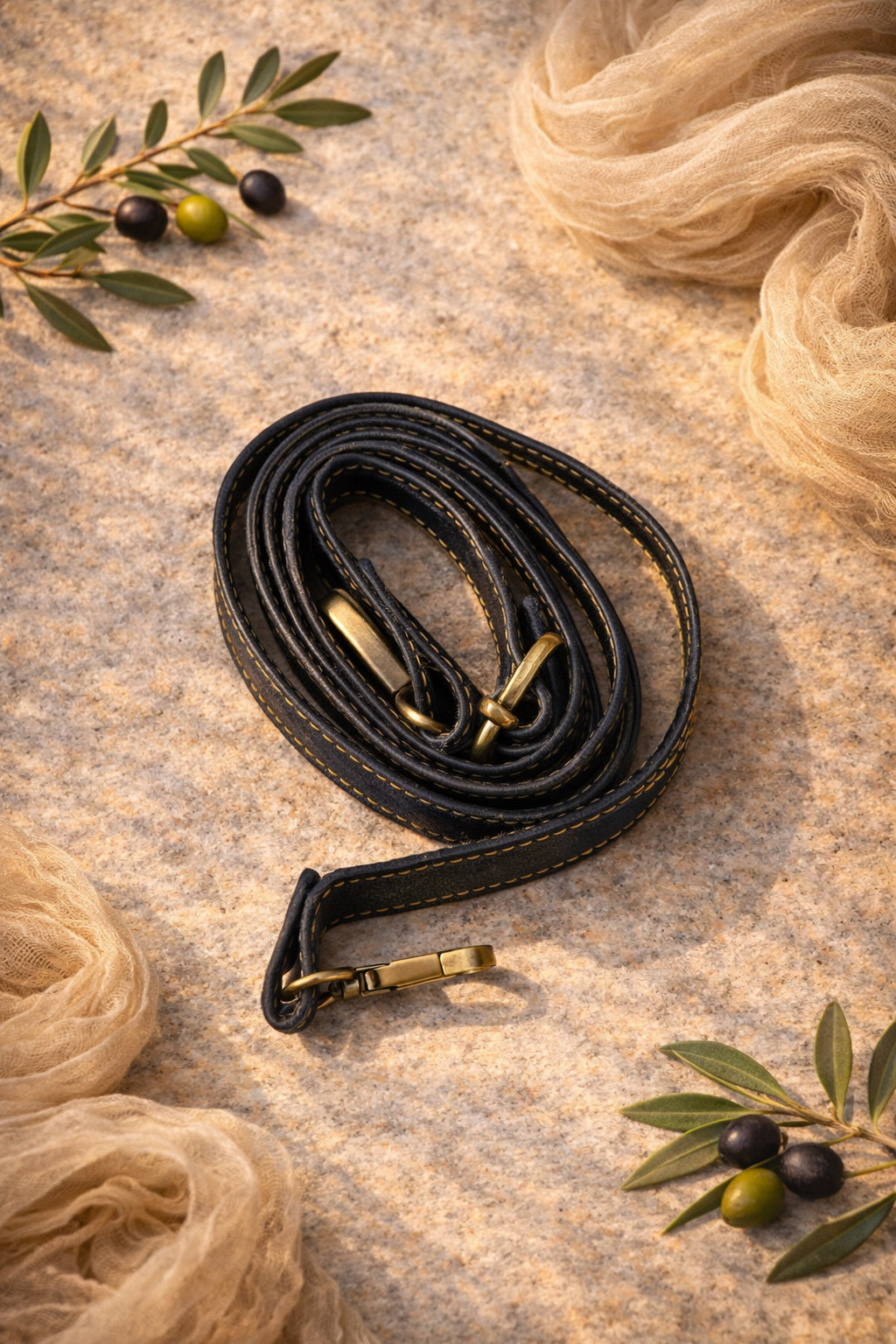 Handmade Leather Crossbody Bag strap displayed on a soft, textured surface with decorative olive leaves.