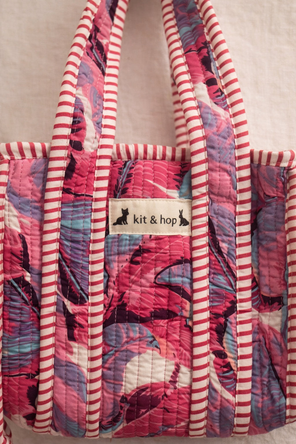Handmade Cotton Mini Tote Bag - Lila - Wild Meadow - Paloma hanging against a wall with floral decorations.