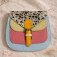 Handmade Leather Crossbody Bag featuring colorful patches of pink, blue, yellow, and a spotted flap on a soft background.