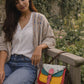 Handmade Leather Crossbody Bag featuring colorful design, model seated on a bench in a garden.