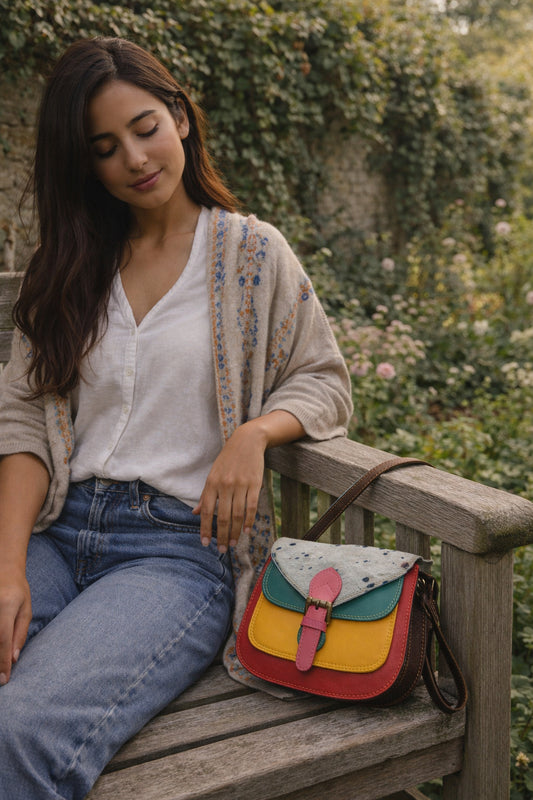 Handmade Leather Crossbody Bag featuring colorful design, model seated on a bench in a garden.