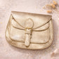 Handmade Leather Crossbody Bag - Romy - Aurelia in metallic gold finish on a sparkling background.