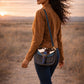 Model wearing a Handmade Leather Crossbody Bag, the Romy, in a scenic outdoor setting at sunrise.