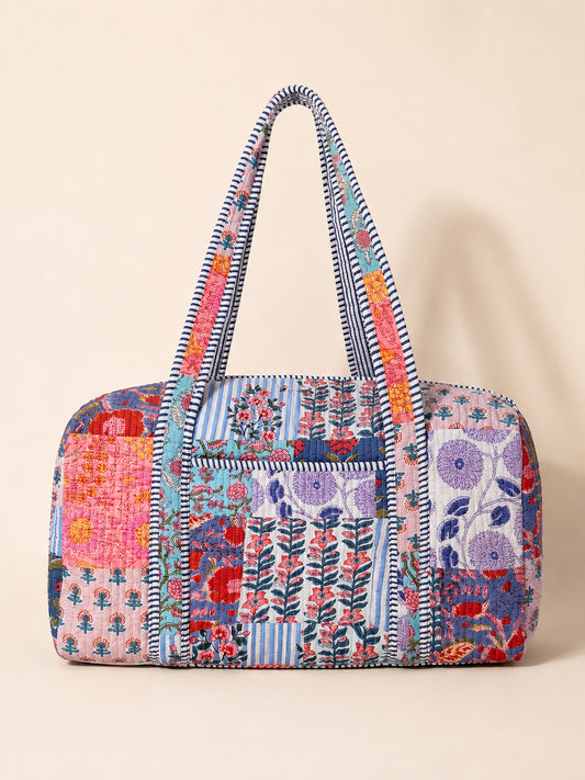 Model carrying a handmade patchwork duffle bag in a colorful flower field under a bright blue sky.