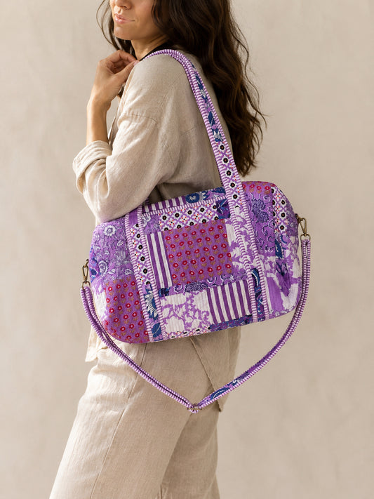 Model carrying a handmade patchwork duffle bag in a colorful flower field under a bright blue sky.